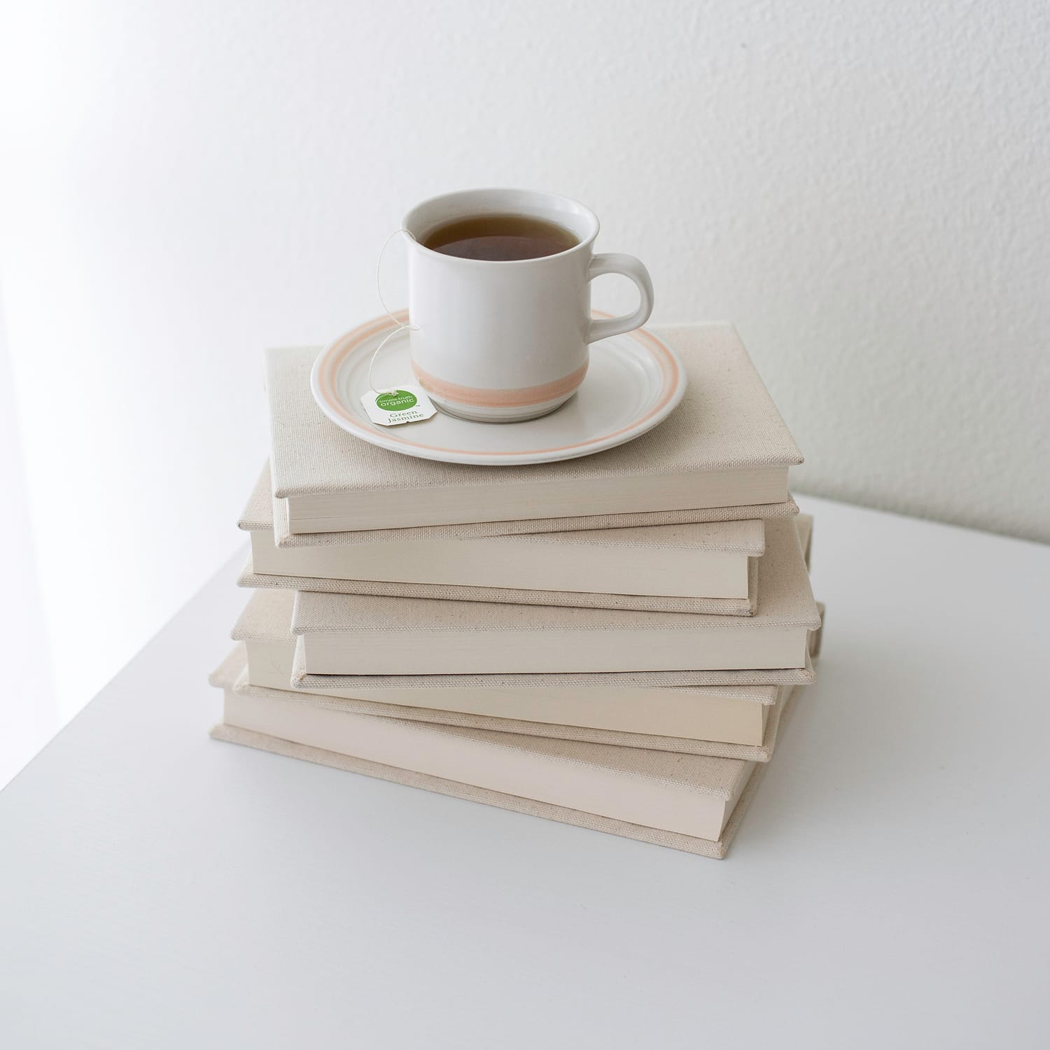 stack of books with no titles showing on a table with a cup of green organic tea on top